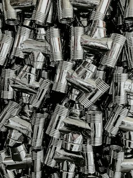 A dense collection of shiny, metallic pipe fittings with threaded sections. The fittings have reflective surfaces and are stacked in an organized, overlapping fashion.