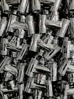 A dense collection of shiny, metallic pipe fittings with threaded sections. The fittings have reflective surfaces and are stacked in an organized, overlapping fashion.