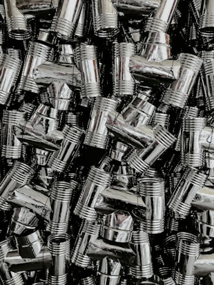 A dense collection of shiny, metallic pipe fittings with threaded sections. The fittings have reflective surfaces and are stacked in an organized, overlapping fashion.