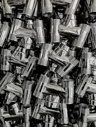 A dense collection of shiny, metallic pipe fittings with threaded sections. The fittings have reflective surfaces and are stacked in an organized, overlapping fashion.