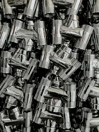 A dense collection of shiny, metallic pipe fittings with threaded sections. The fittings have reflective surfaces and are stacked in an organized, overlapping fashion.