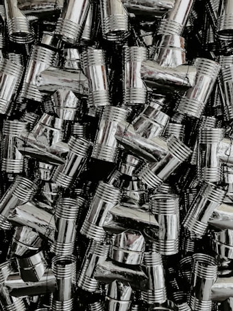 A dense collection of shiny, metallic pipe fittings with threaded sections. The fittings have reflective surfaces and are stacked in an organized, overlapping fashion.