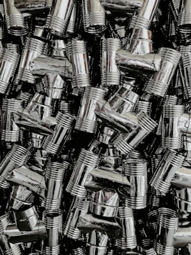 A dense collection of shiny, metallic pipe fittings with threaded sections. The fittings have reflective surfaces and are stacked in an organized, overlapping fashion.