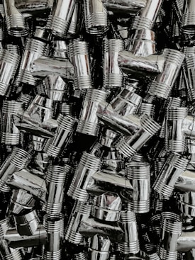 A dense collection of shiny, metallic pipe fittings with threaded sections. The fittings have reflective surfaces and are stacked in an organized, overlapping fashion.