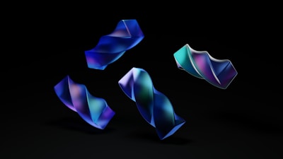 Several abstract, twisted shapes with a smooth, glossy texture float against a dark background. The shapes exhibit a gradient of colors, primarily in shades of blue, purple, and teal, giving a futuristic and dynamic appearance.