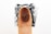 A close-up of a fingertip with a visible fingerprint pattern. The background is blurred and appears to have a dark ink stamp or smudge behind the finger.
