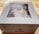 A white box labeled 'Colorado Cherry Co.' is on a wooden surface. The box has a clear window on top, revealing a partially visible baked good inside, possibly topped with sugar.