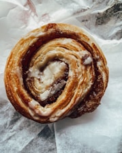 Close-up photo of a cinnamon roll with icing on a rustic wooden table.
