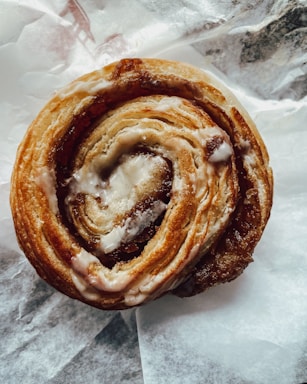Close-up photo of a cinnamon roll with icing on a rustic wooden table.