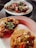 Three plates of tacos, each topped with a variety of ingredients including meats, chopped onions, cilantro, sliced radishes, and pickled jalapeños. The tacos are presented on corn tortillas and are arranged on simple white plates, sitting on a dark surface.
