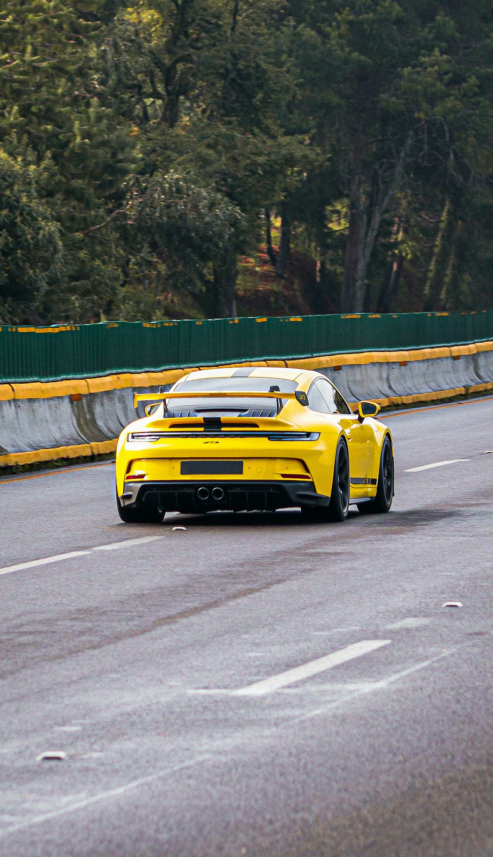 a yellow and black race car on a road with trees on the side