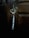 A metallic key hangs from a heart-shaped keyring inserted into a lock on a wooden door. The background is dimly lit, emphasizing the rustic texture and dark color of the wood.