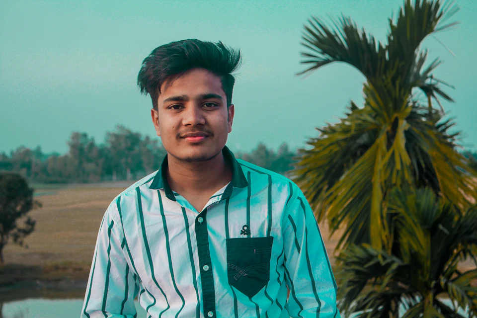 Young man stands in a lush green field with a white and black striped shirt