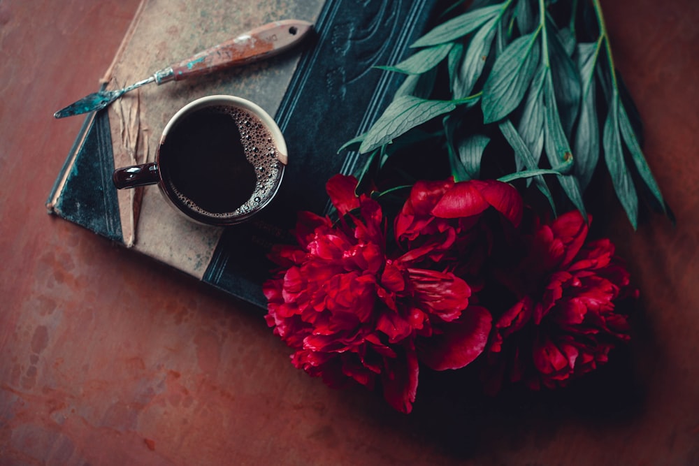 Un ramo de flores rojas junto a una taza de café