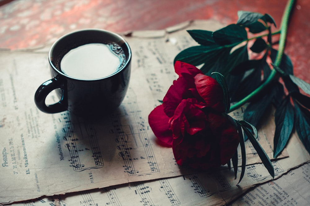 a cup of coffee next to a rose