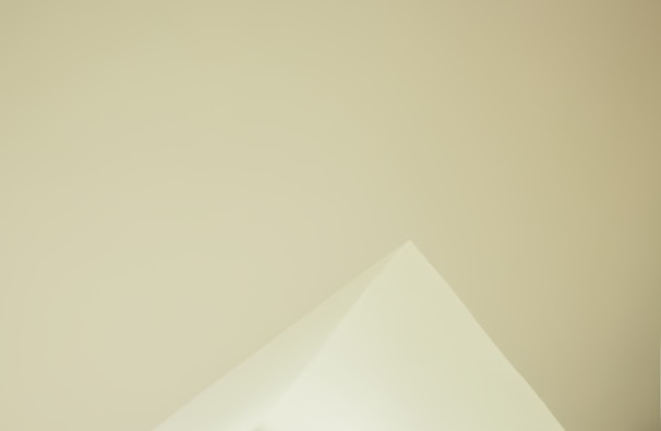 A minimalistic image featuring the corner of a triangular paper against a smooth, light beige background. The sharp angles and soft color tones create a sense of simplicity.