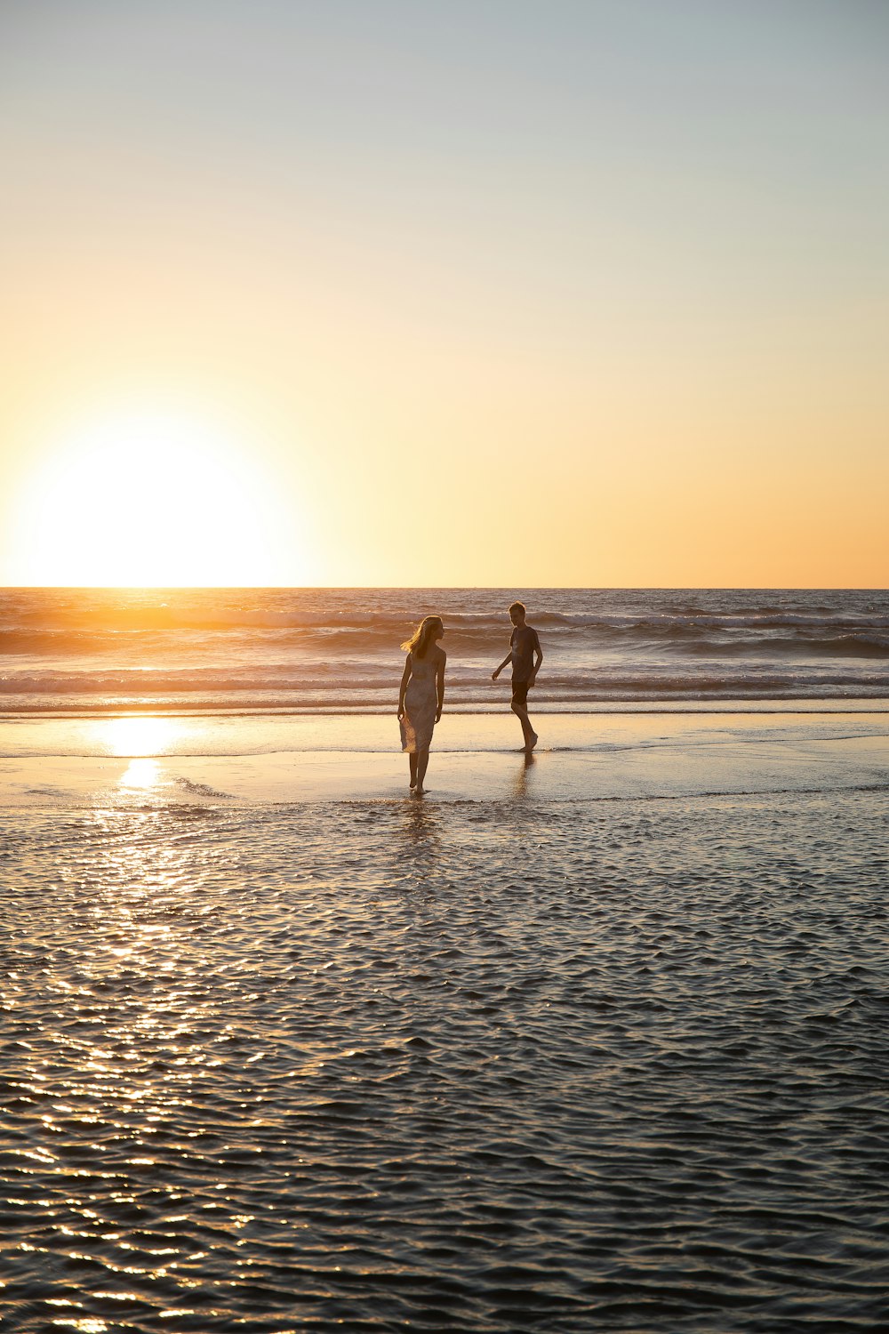 a man and woman walking on a beach at sunset