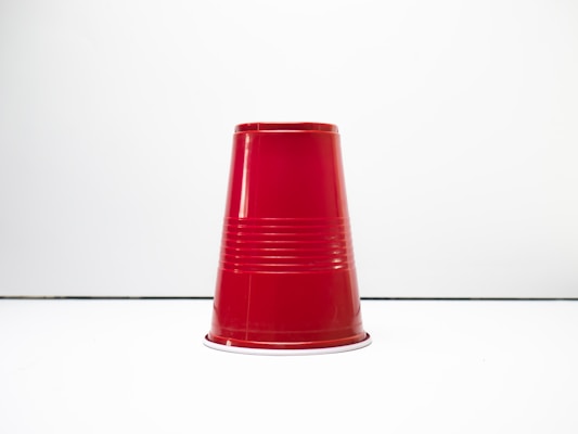 A red plastic cup is positioned upside down on a plain white surface. The cup has a glossy finish and distinctive ridges along its body, adding texture to the otherwise smooth surface.