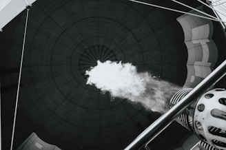 The image captures the interior of a hot air balloon from the perspective inside the balloon's envelope. A burner is releasing a blast of flame upwards, inflating the balloon. The fabric of the balloon envelops the space, and the concentric lines create a dramatic focal point.
