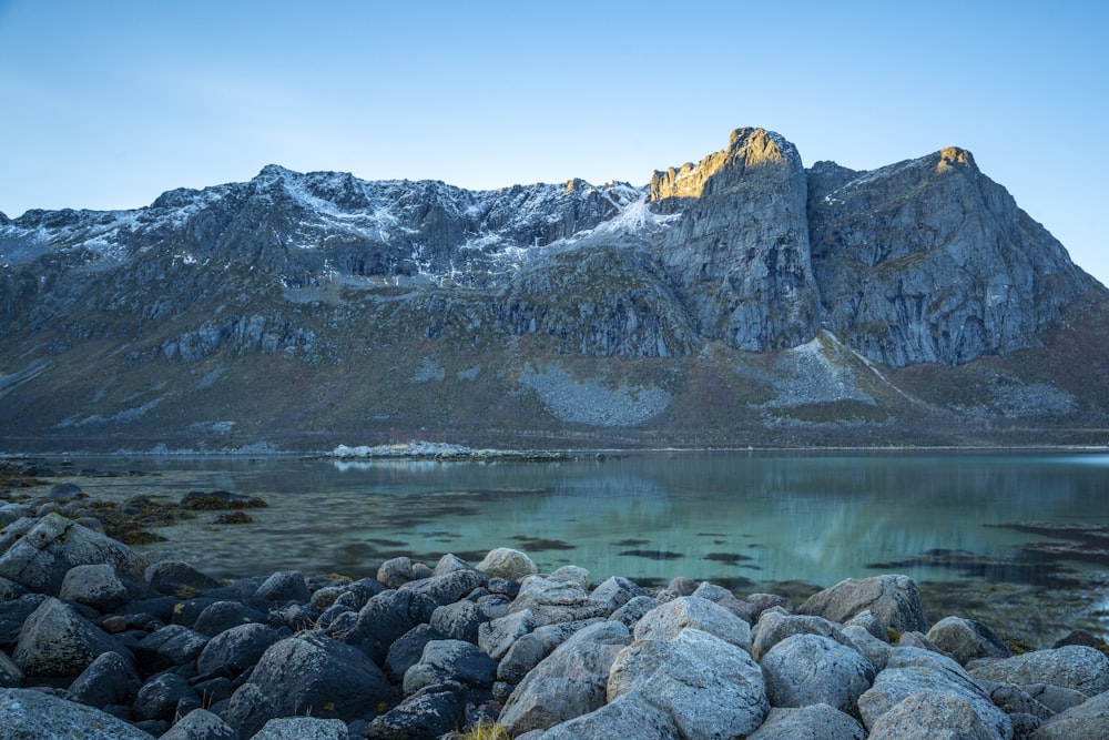 a rocky shore with a body of water and mountains in the background