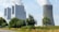 A large industrial facility with multiple tall structures emitting white smoke is situated next to a cooling tower. The facility is surrounded by greenery, including trees and grass, and there is a road running along the side.