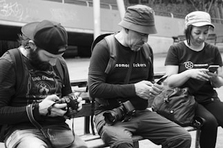 a group of people sit on a bench looking at their phones