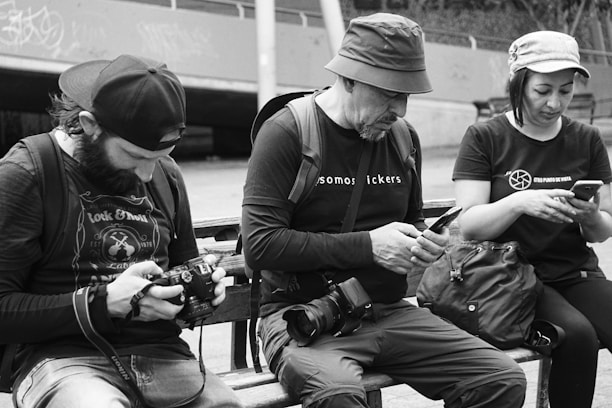 a group of people sit on a bench looking at their phones