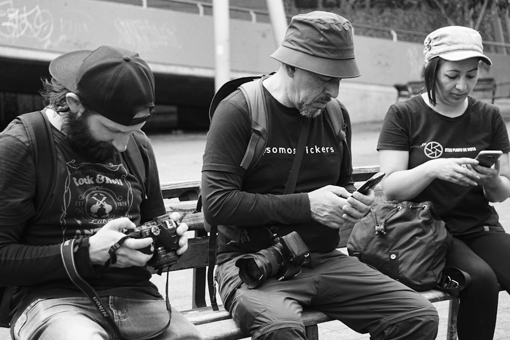 a group of people sit on a bench looking at their phones