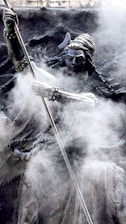 A detailed sculpture of a figure with an ornate headdress, holding a long staff or spear, enveloped in swirling mist or smoke. The intricate carvings and flowing robes add to the mystical and ancient appearance.