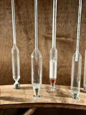 Several narrow glass tubes with varying amounts of granular material are mounted vertically on a wooden base. Each tube features measurement marks, suggesting a scientific or laboratory setting.