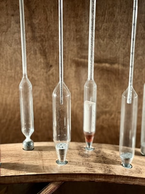 Several narrow glass tubes with varying amounts of granular material are mounted vertically on a wooden base. Each tube features measurement marks, suggesting a scientific or laboratory setting.