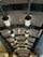 A series of modern, industrial-style lamps hanging from a curved, metallic ceiling with a grid pattern. The ceiling structure is lined with dark, arched beams and the lighting casts a warm glow on the surroundings.