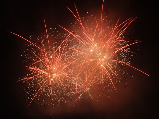 Bright red and orange fireworks burst across a dark night sky, creating a dazzling display of sparks and light trails.