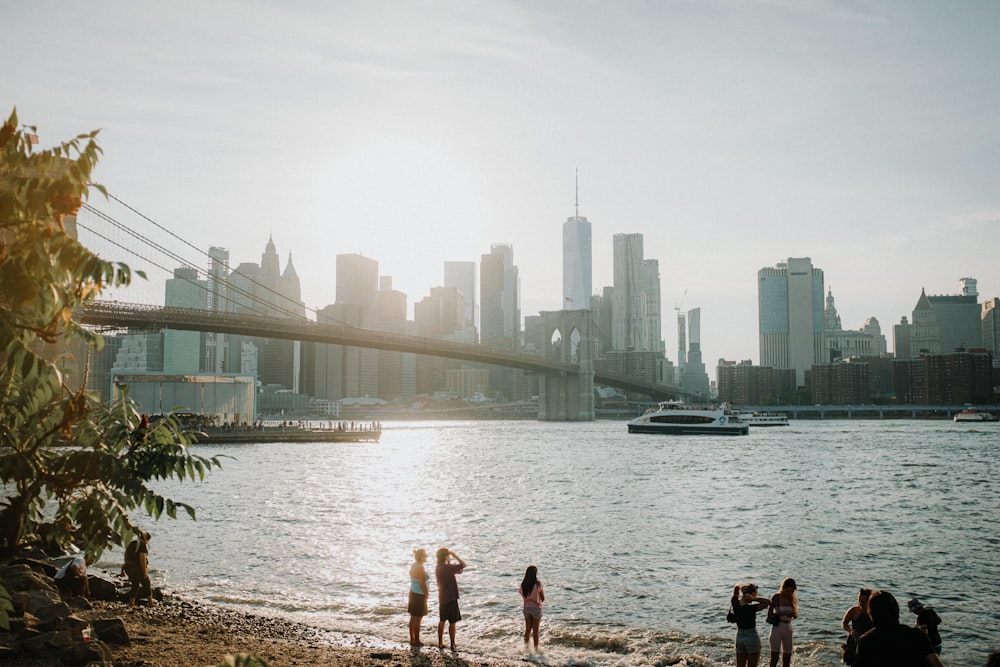 a group of people standing on a rocky shore by a body of water with a bridge and a