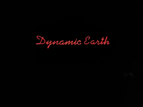 Red neon text spells out 'Dynamic Earth' against a completely black background.