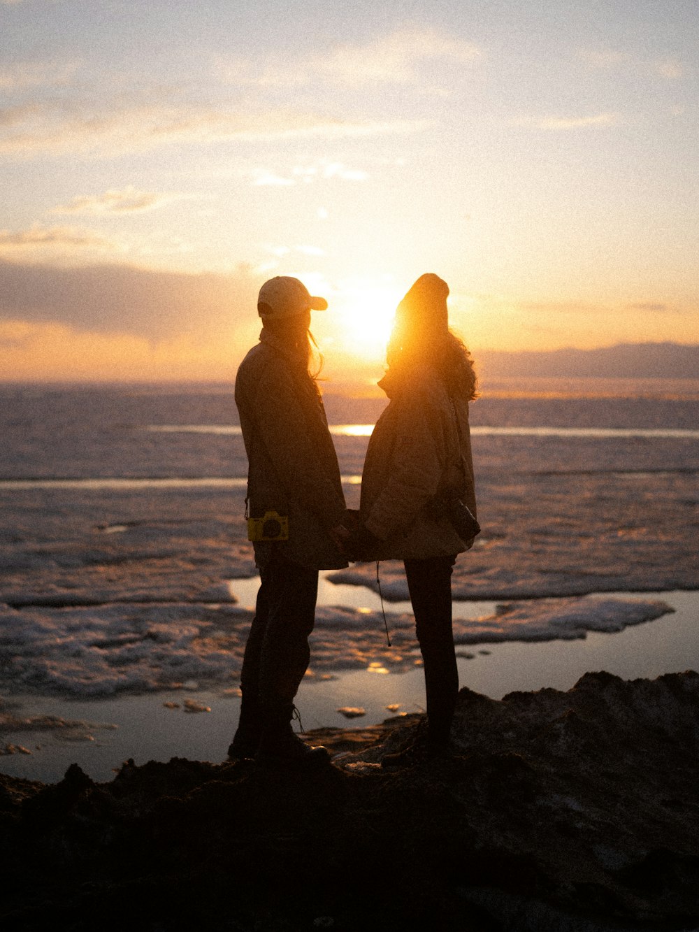 a couple of people standing on a beach looking at the sunset