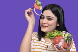 a woman holding a strawberry and a bowl of fruit