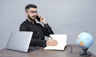 a man holding a pen and a book and a laptop