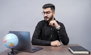 a man sitting at a desk with a laptop and a globe
