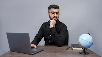 a man sitting at a desk with a laptop and a globe