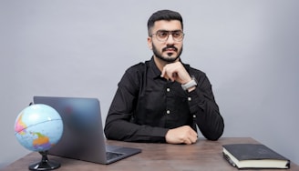 a man sitting at a desk with a laptop and a globe