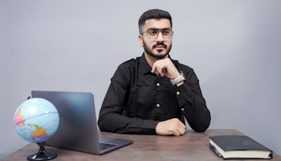 a man sitting at a desk with a laptop and a globe