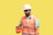 A male construction worker wearing a white hard hat and orange safety vest is holding an orange case. He is looking at the case, standing against a plain yellow background. The worker is also wearing a blue shirt under the vest.