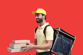 a man in a yellow hat holding a box and a laptop