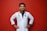 A smiling person in a white lab coat stands confidently against a solid red background, with hands on their hips. A stethoscope hangs around the neck, suggesting a medical professional.