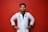 A smiling person in a white lab coat stands confidently against a solid red background, with hands on their hips. A stethoscope hangs around the neck, suggesting a medical professional.