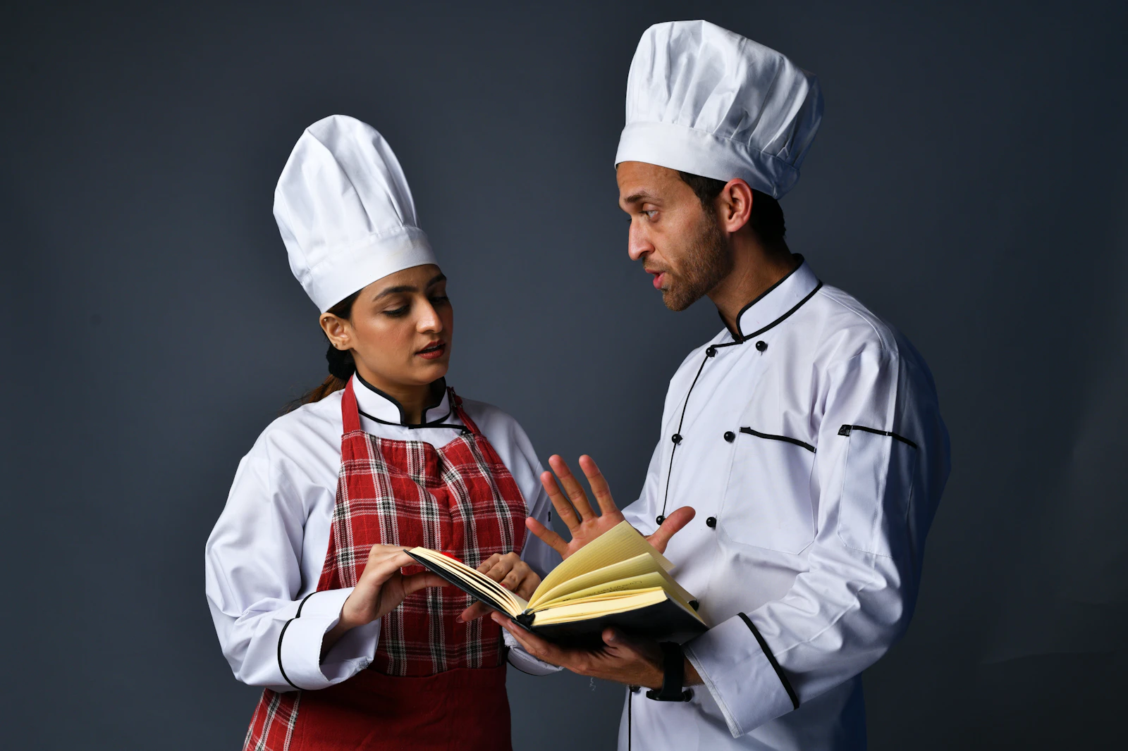 A male and a female chef in uniforms reviewing a plated dish together