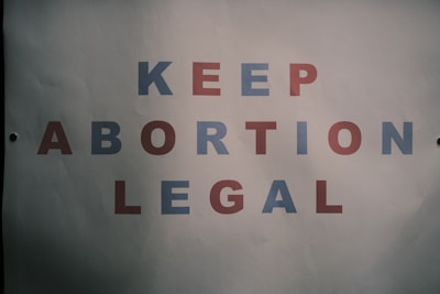A poster with text saying 'KEEP ABORTION LEGAL.' The letters are in alternating colors of blue and red, displayed against a plain white background.