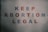 A poster with text saying 'KEEP ABORTION LEGAL.' The letters are in alternating colors of blue and red, displayed against a plain white background.