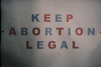 A poster with text saying 'KEEP ABORTION LEGAL.' The letters are in alternating colors of blue and red, displayed against a plain white background.